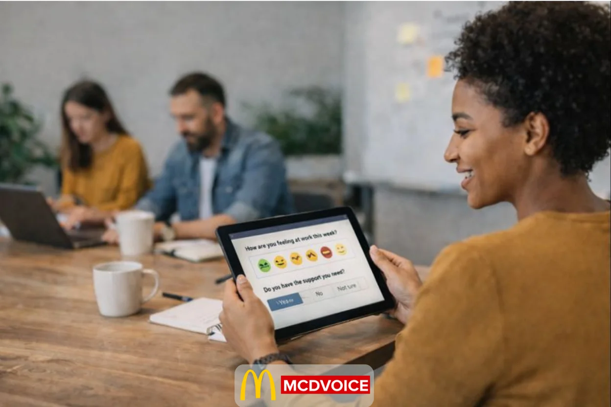 Employee completing a pulse survey on a tablet while coworkers work together in a modern office.